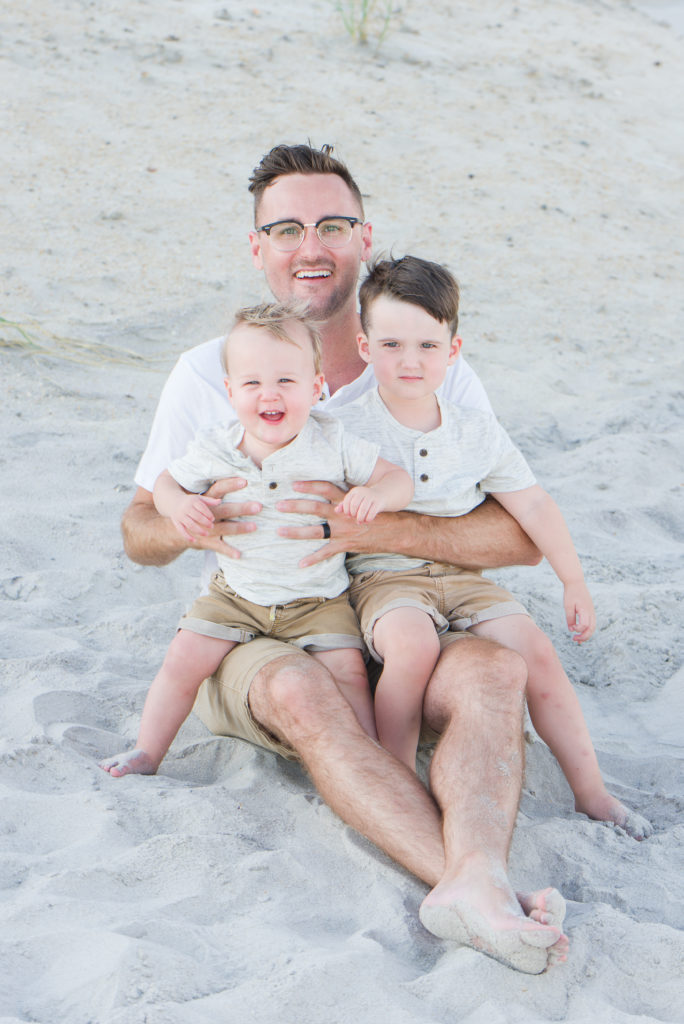 father holding boys on beach