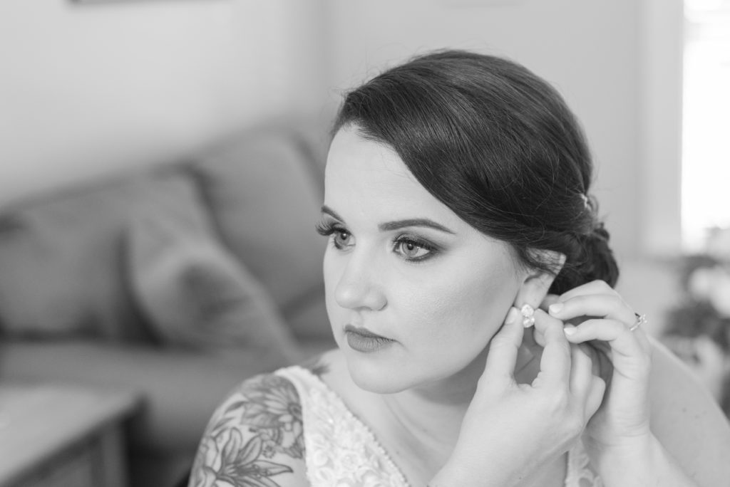 black and white photo of bride putting on earrings