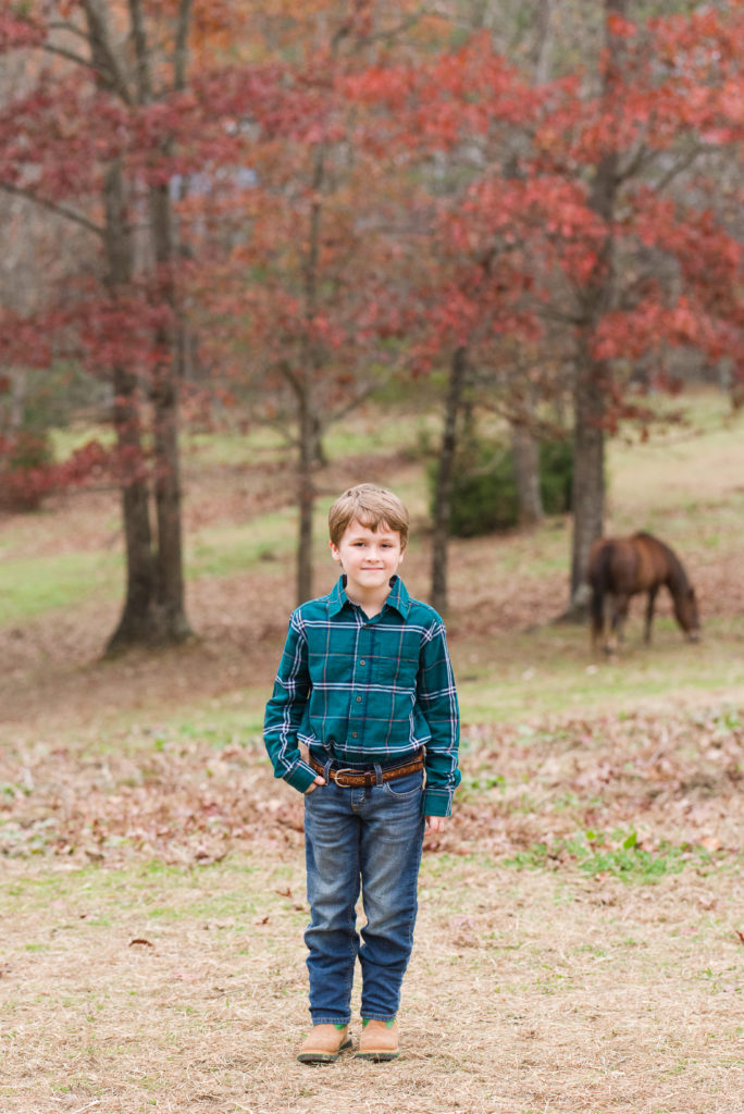 child posing in pasture with horse behind him