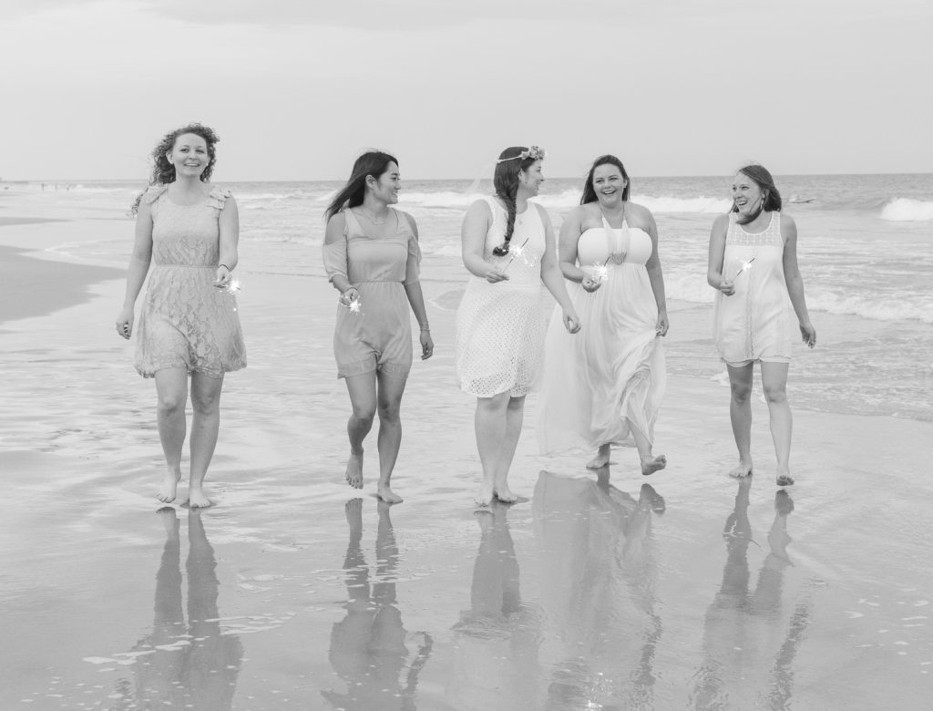 bride and bridesmaids walking down beach with sparklers