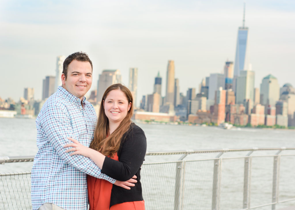 engaged couple standing in front of New York Skyline at Pier A Park Hoboken