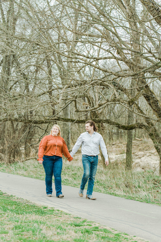 engaged couple walking on path beside riverbank