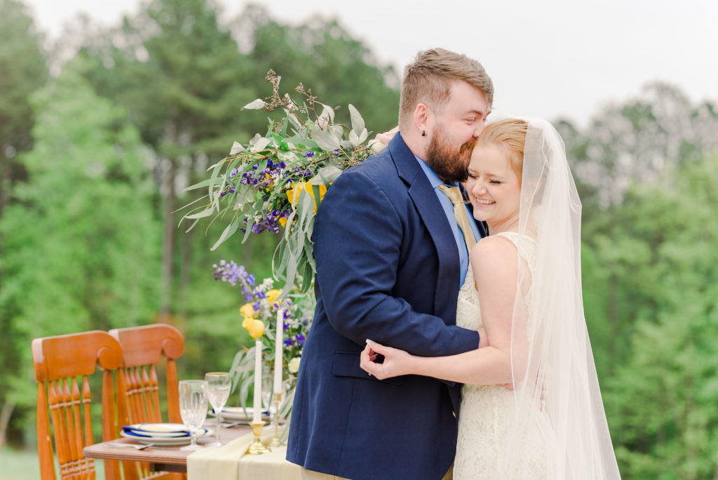 groom nuzzling laughing bride in front of blue and yellow themed sweetheart table