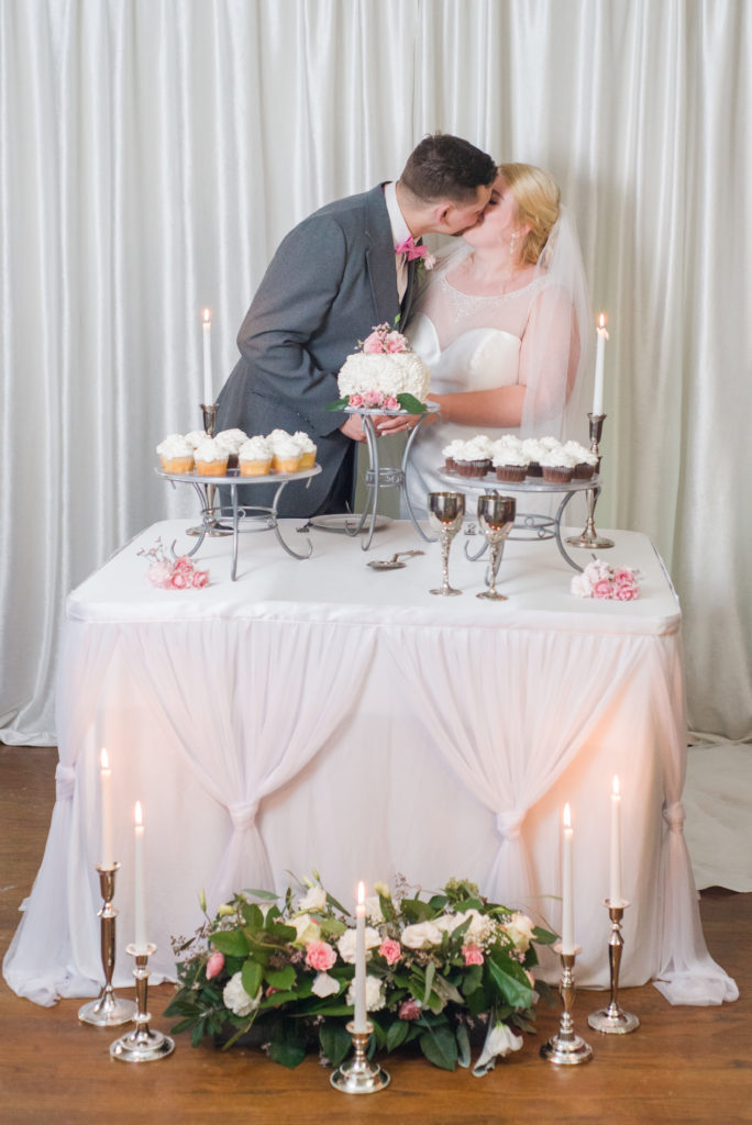 bride and groom kissing while cutting wedding cake