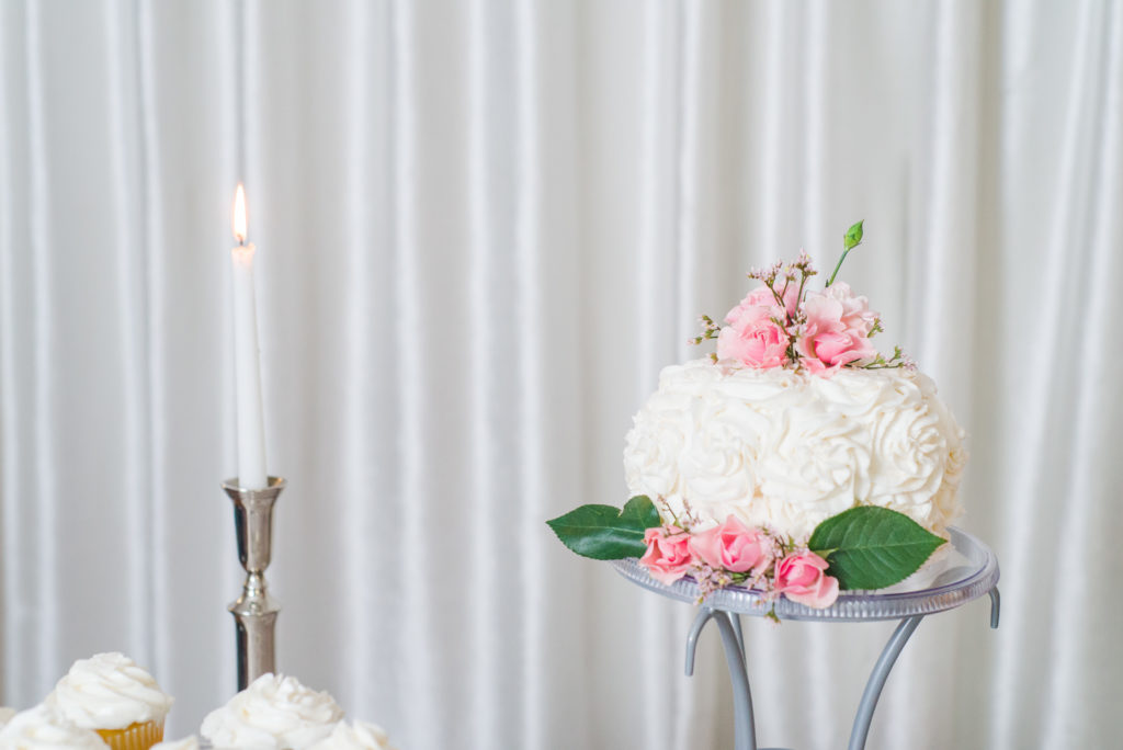 white wedding cake with pink flowers and greenery and silver candlestick
