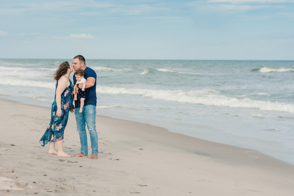 couple kissing on the beach with their infant son