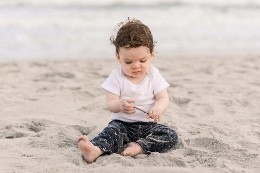 infant playing with stick while sitting on the beach