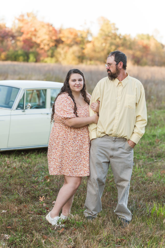 couple in a field with antique car and fall foliage