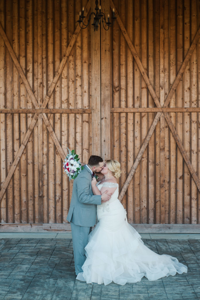 couple kissing in front of barn doors after their wedding at Wright Memorial Event Center