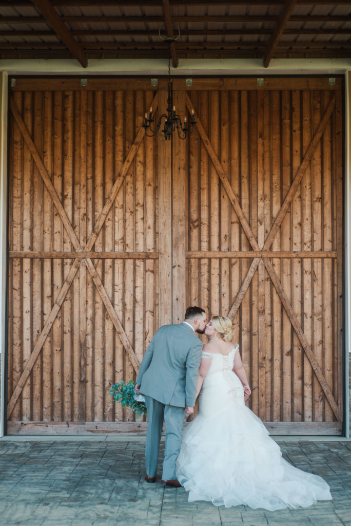 couple kissing in reverse v pose in front of large barn doors before wedding