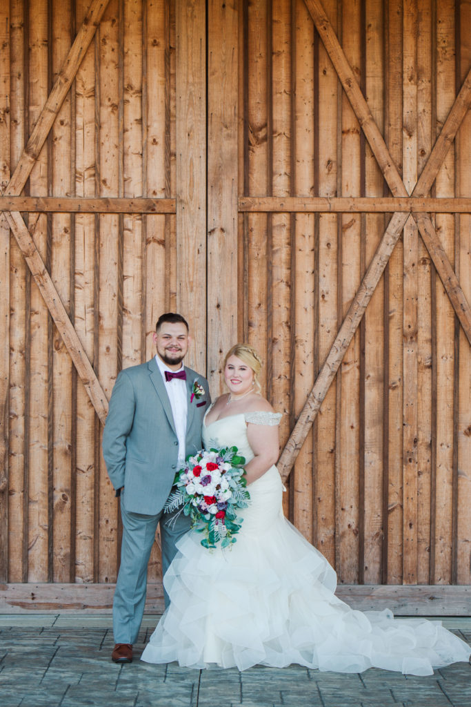couple in traditional cake topper pose in front of barn doors