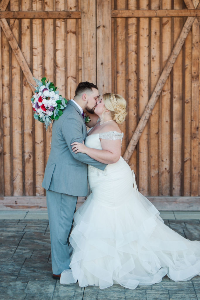 couple kissing in front of barn door during wedding portraits