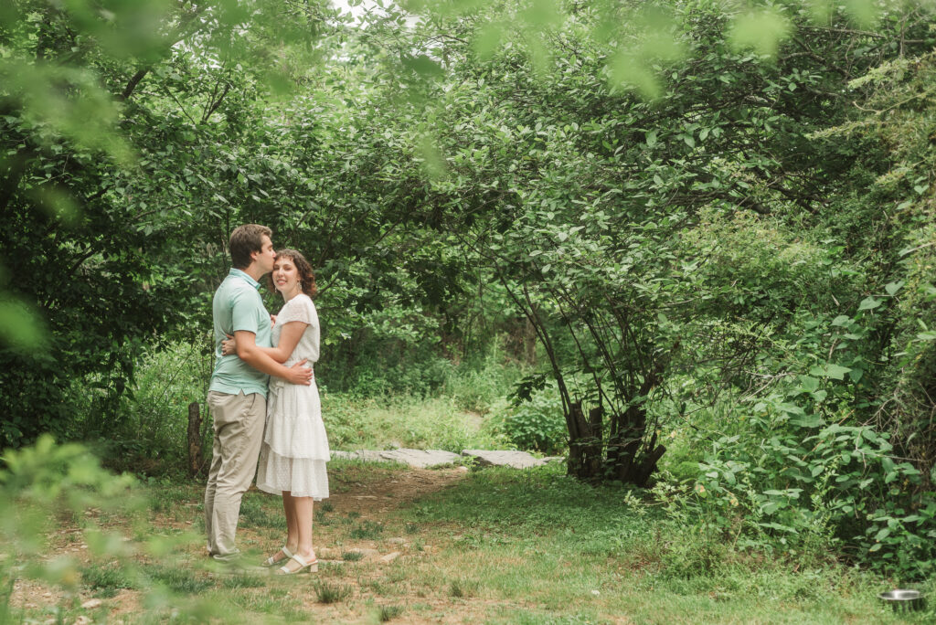 Couple embracing in front of South Fork Rockfish River during Engagement Session at Bold Rock Hard Cider, Nellysford, Virginia