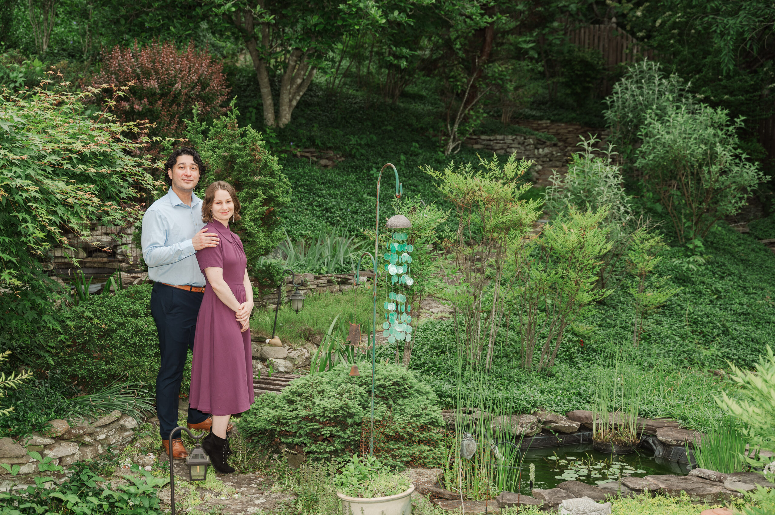 Engaged couple standing by small garden pond