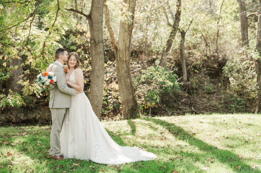 Groom holding the bride close with fall colors in the background.