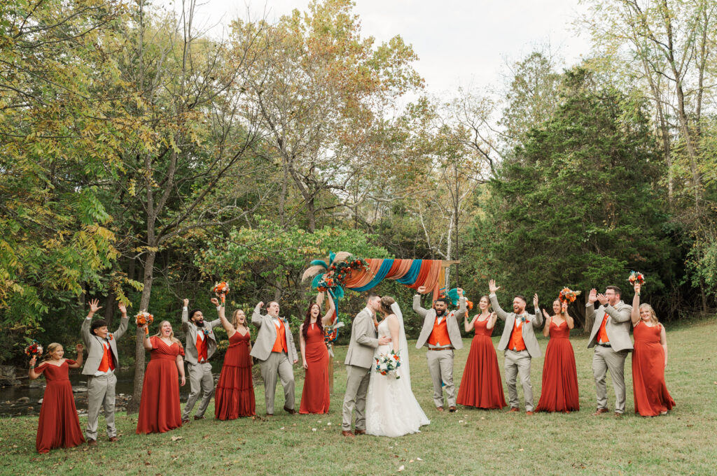 wedding party cheering at bride and groom kissing by the river