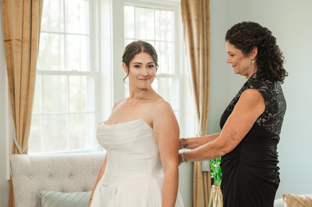 bride getting zipped in dress by mother