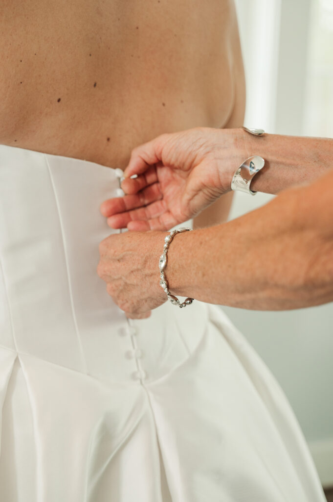 bride getting zipped in dress by mother