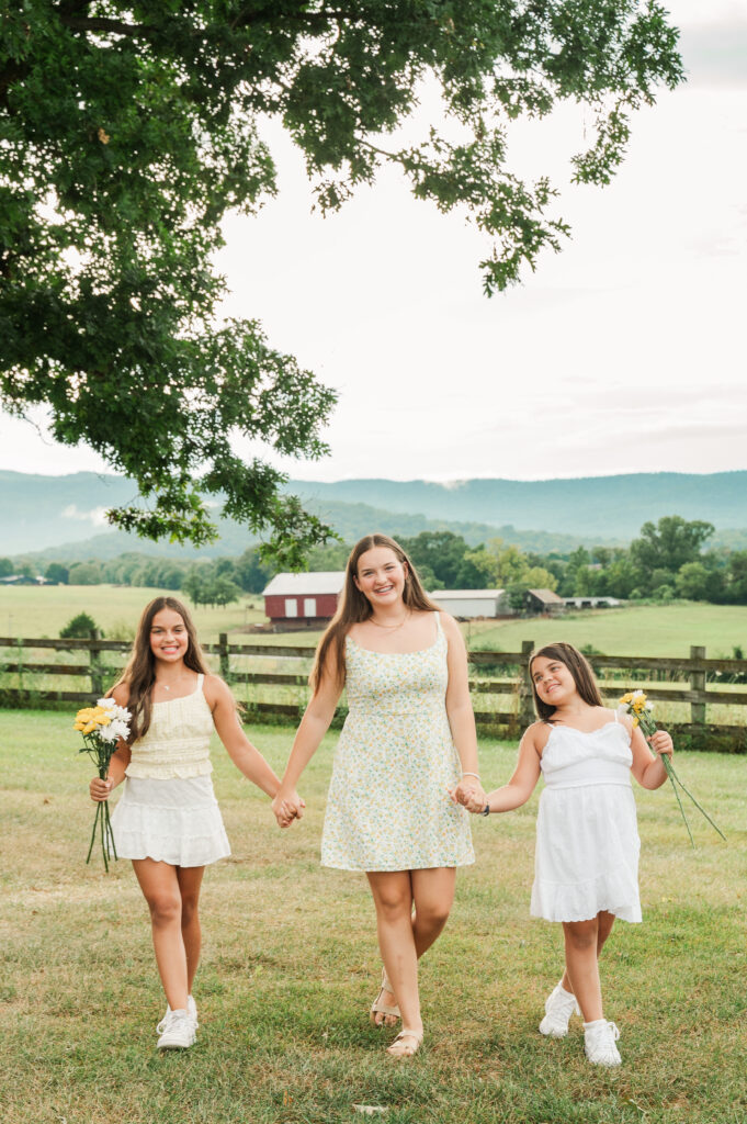 3 granddaughters walking and laughing while holding hands and carrying daisies