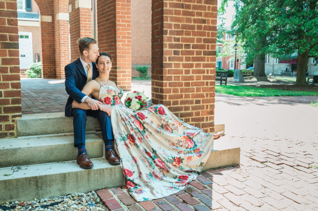 groom kissing bride's temple while seated on steps