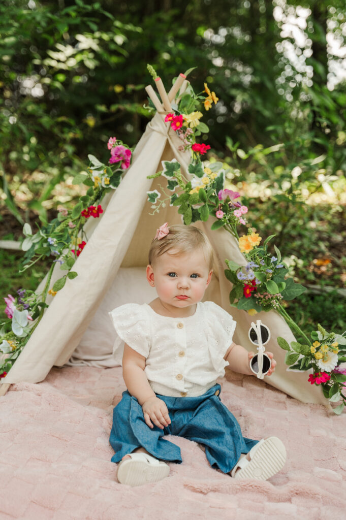 Teagan sitting on blanket with teepee adorned with florals