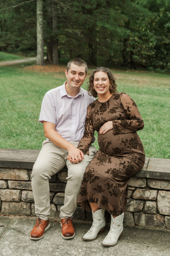Full-length photo of Emilyand Derek sitting comfortably on a rock wall, showing off her fitted dress and white boots