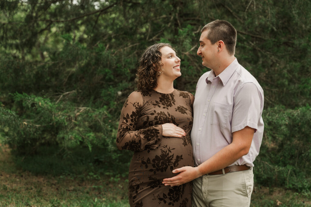 Emily and Derek laughing while holding Emily's bump during their fall maternity session
