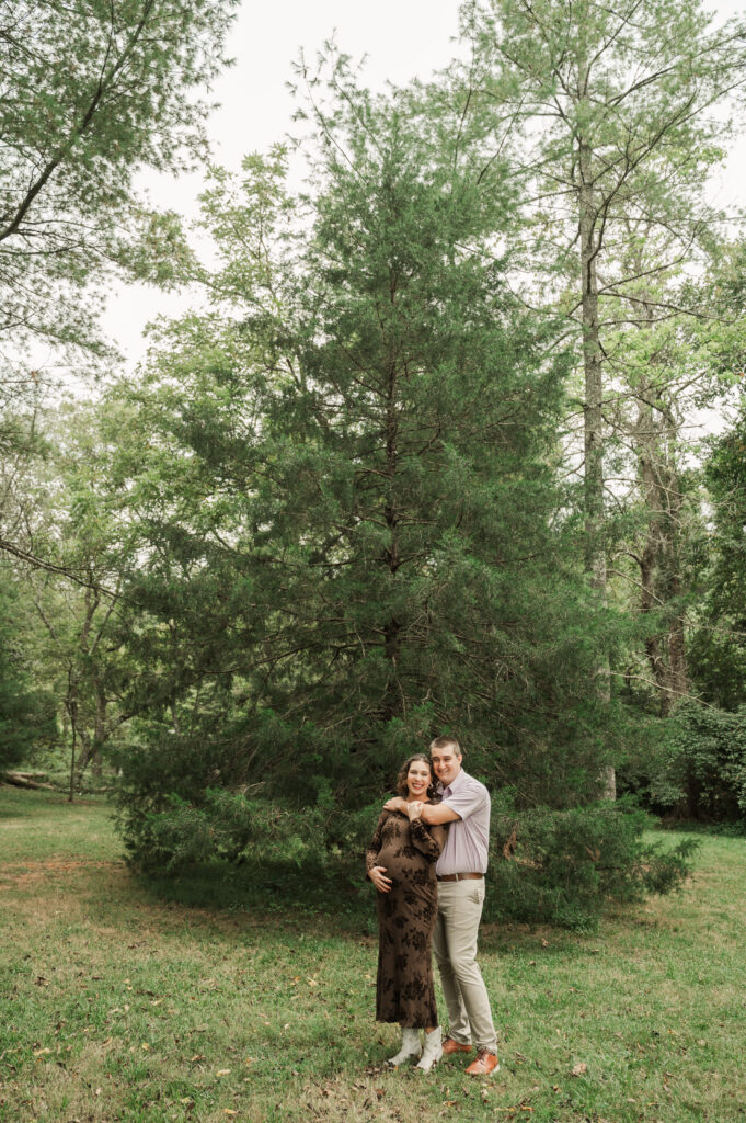 Emily & Derek standing in front of large tree during their fall maternity session