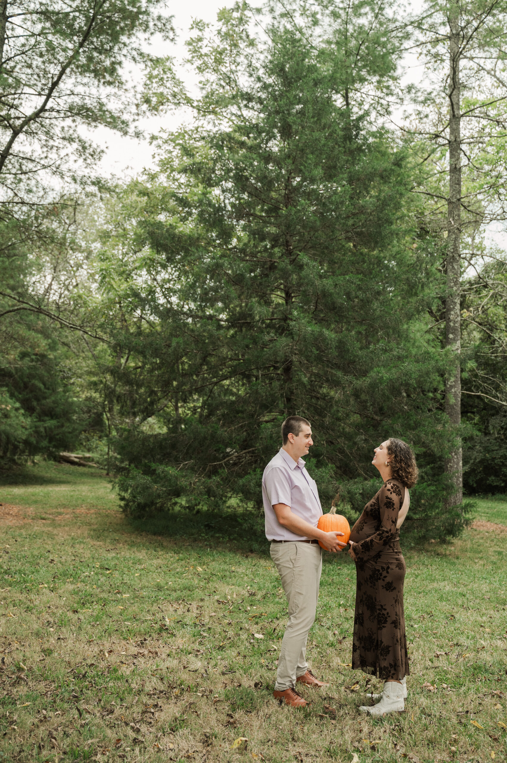 Playful maternity photo on the Saunders-Monticello Trail with Derek holding a pumpkin as his own 'bump,' next to pregnant Emily