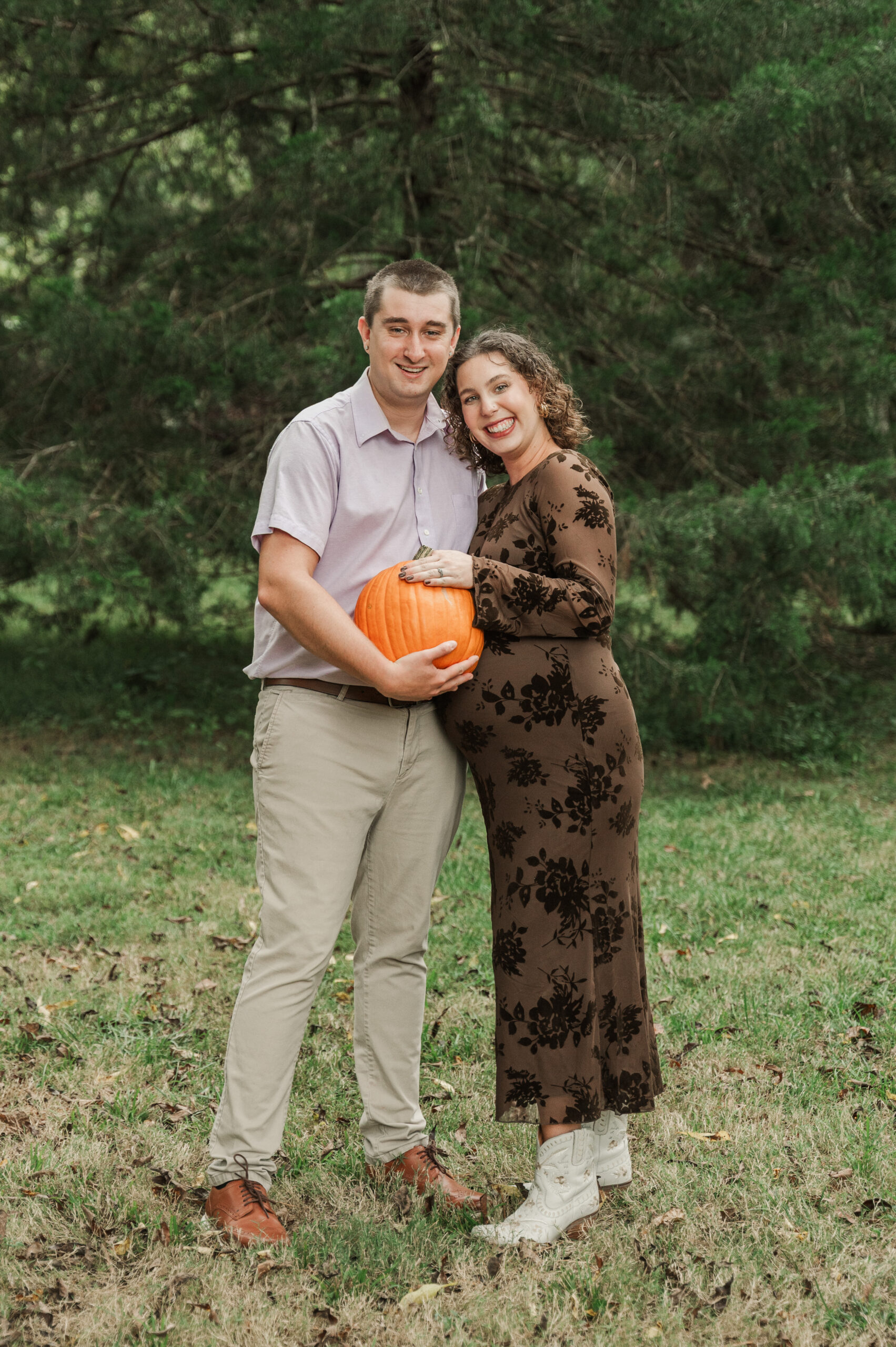 Playful maternity photo on the Saunders-Monticello Trail with Derek holding a pumpkin as his own 'bump,' next to pregnant Emily