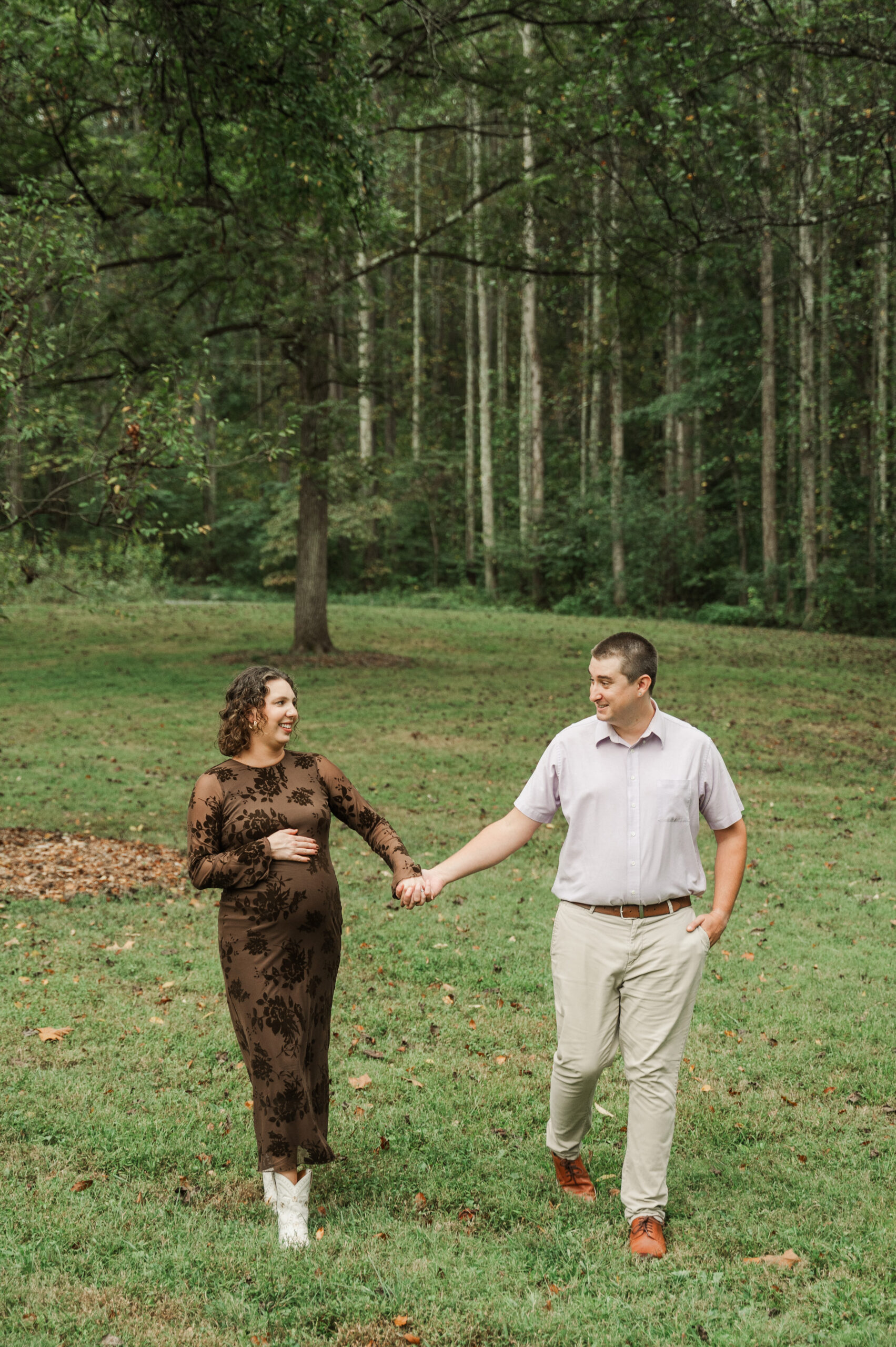 A walking maternity shot capturing the modern style of Emily's white boots paired with her fitted dress as she walks with Derek