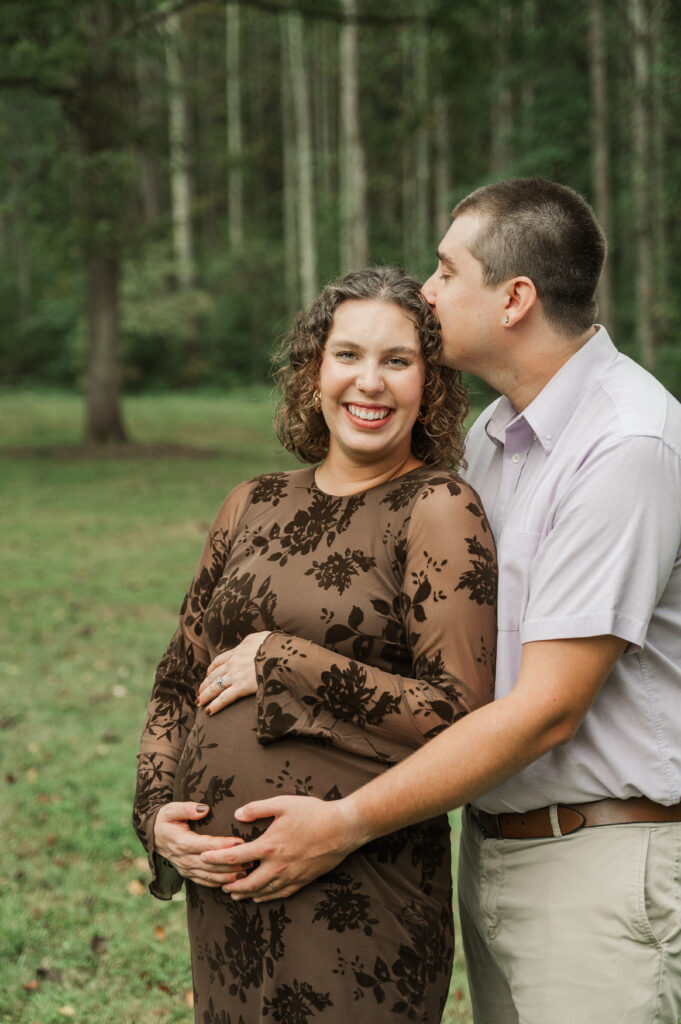 Derek kissing Emily on the top of her head while they hold their baby bump