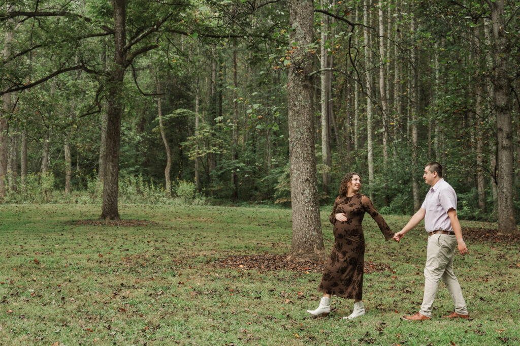 Pregnant Emily and Derek walking hand-in-hand down the gravel Saunders-Monticello Trail on a soft, overcast afternoon