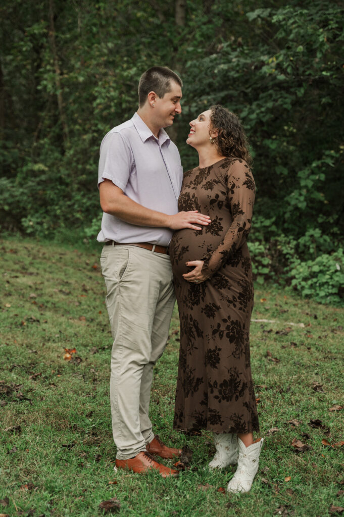 Pregnant woman Emily wearing a fitted maternity dress and white boots posing with husband Derek at Saunders-Monticello Trail in September.