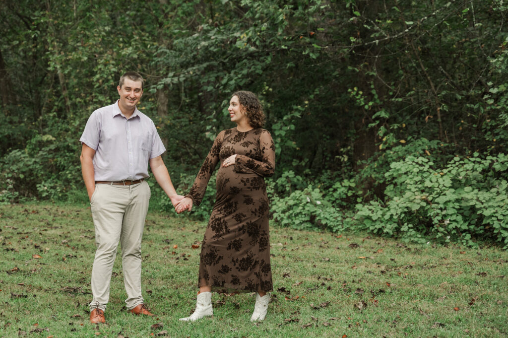 Pregnant Emily and Derek standing hand-in-hand at Saunders-Monticello Trail on a soft, overcast afternoon