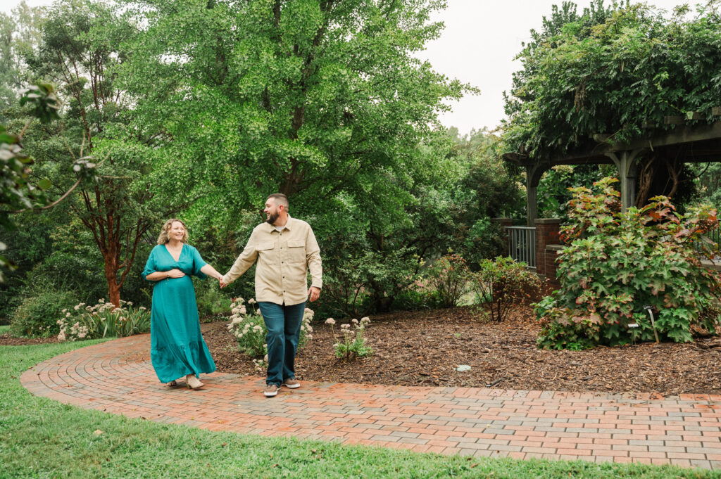 Expecting parents walking through the lush green fields of Tanglewood Park in North Carolina.
