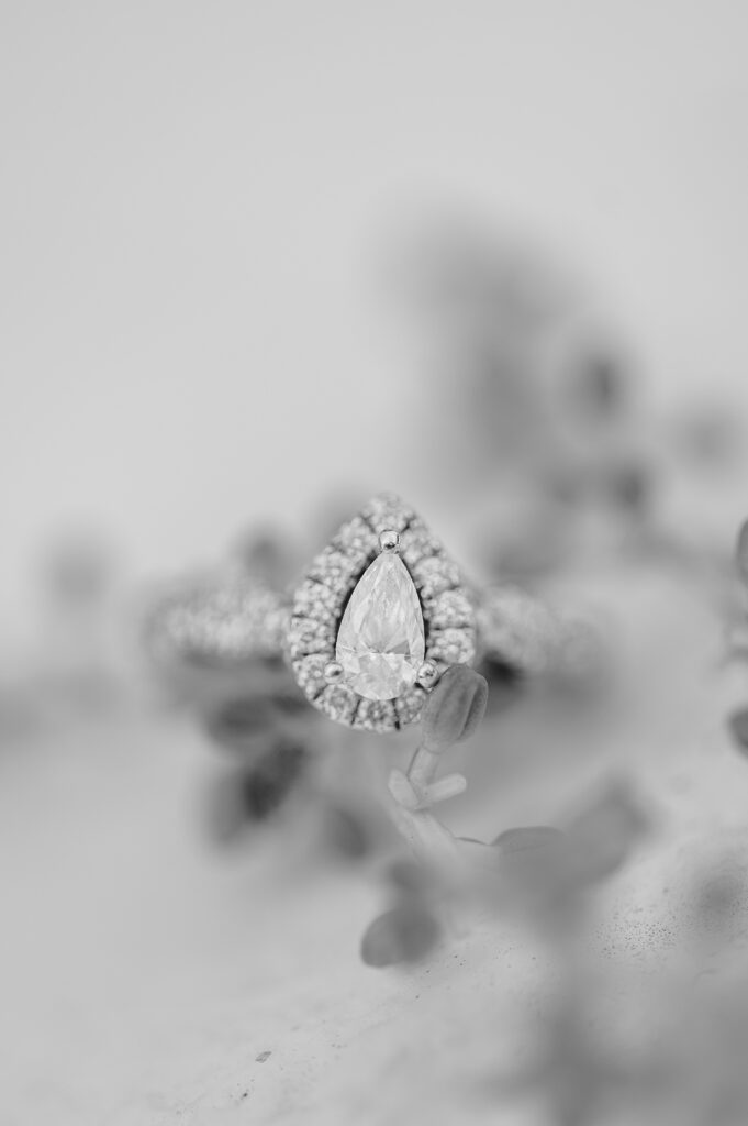 black and white image of pear shaped engagement ring laying on tiny flowers