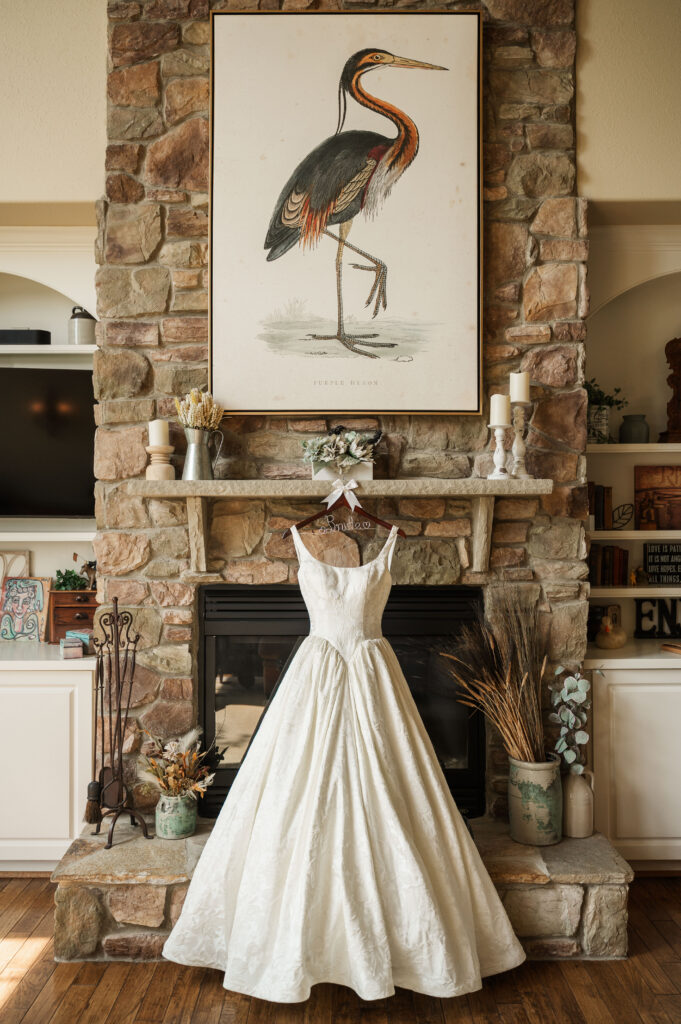 ivory woven floral jacquard wedding gown hanging on stone fireplace