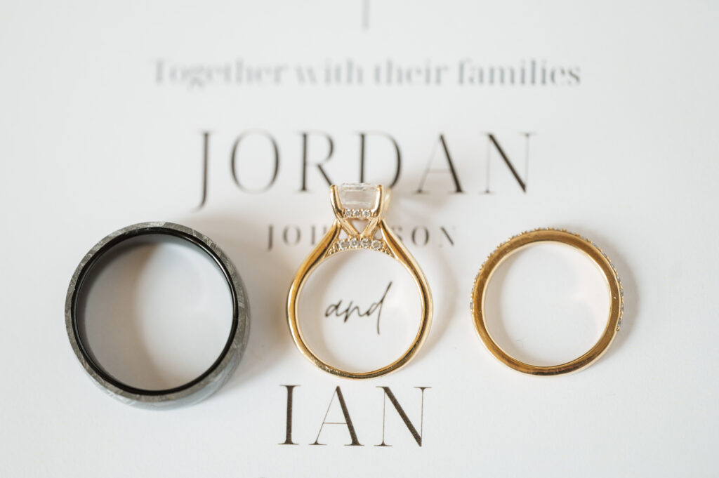 Jordan & Ian's wedding rings laying on invitation between their names